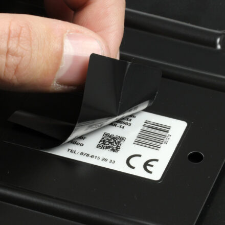 Close-up van een hand die het beschermlaminaat van een PaintLabel verwijdert na poedercoaten