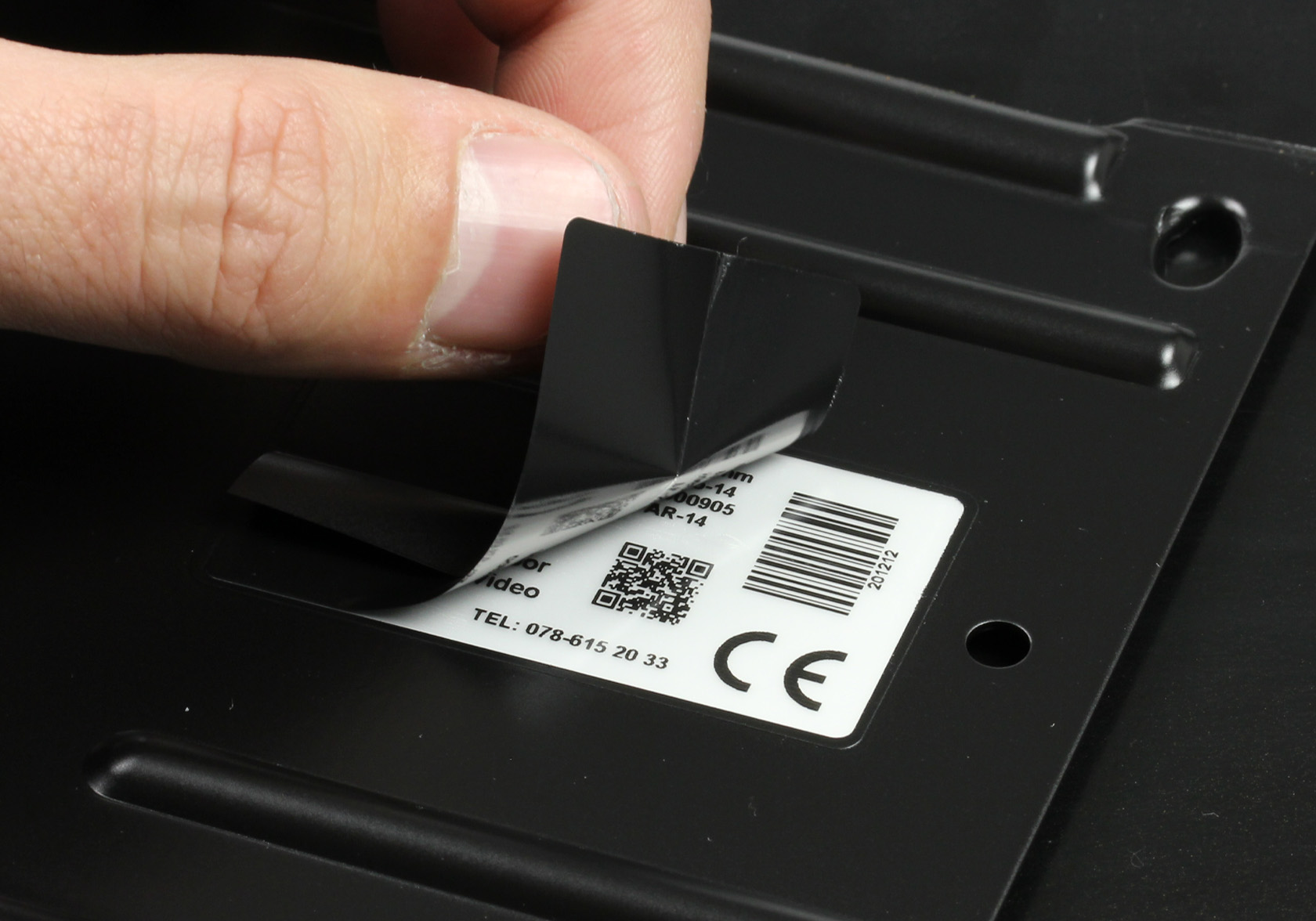 Close-up van een hand die het beschermlaminaat van een PaintLabel verwijdert na poedercoaten