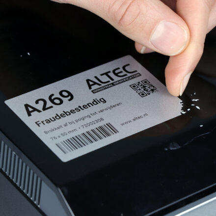 Close-up van een hand die een fraudebestendig label verwijdert, waarbij het label in kleine stukjes afbrokkelt om vervalsing te voorkomen