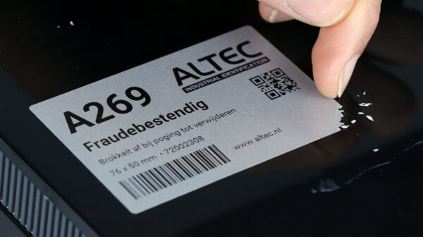 Close-up van een hand die een fraudebestendig label verwijdert, waarbij het label in kleine stukjes afbrokkelt om vervalsing te voorkomen